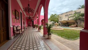 A corridor with pink walls, a patterned floor, and a fountain in the courtyard. - La Casa Rosa Imperial (Mérida)