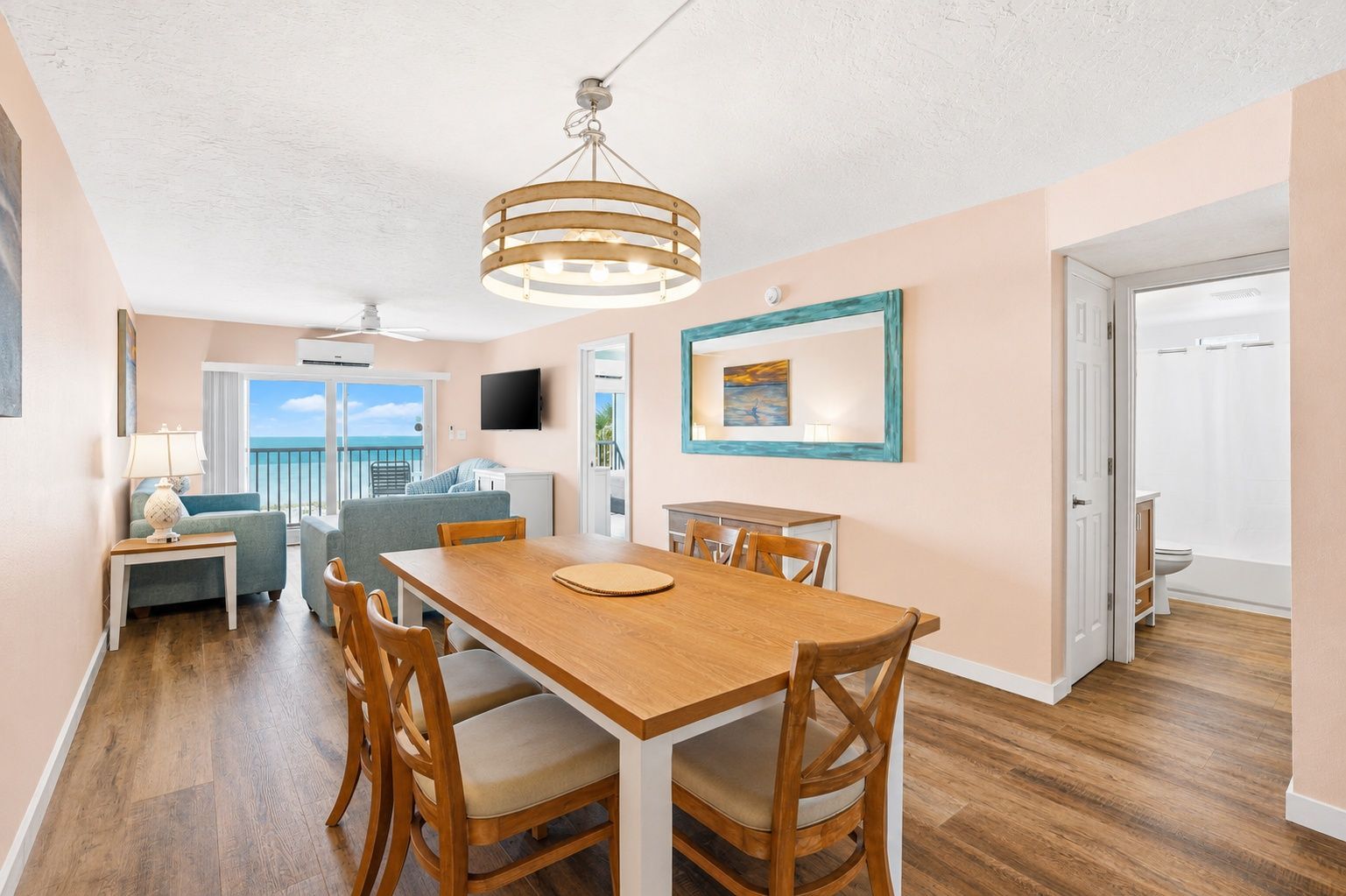 A dining area with a wooden table and chairs, a ceiling light fixture, and a view of the ocean through a balcony door.