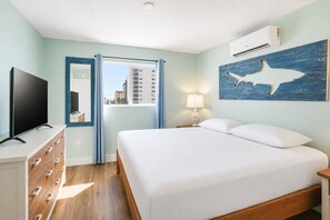 Habitación de hotel con cama, televisor, cómoda, ventana con cortinas y aire acondicionado instalado en la pared.