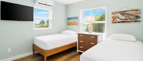 Un dormitorio con dos camas individuales, un aparador de madera, ventilador de techo, equipo de aire acondicionado y televisor montado en la pared.