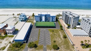 Ein Strandhotel mit mehreren Gebäuden, einem grünen Tennisplatz und einem Parkplatz.