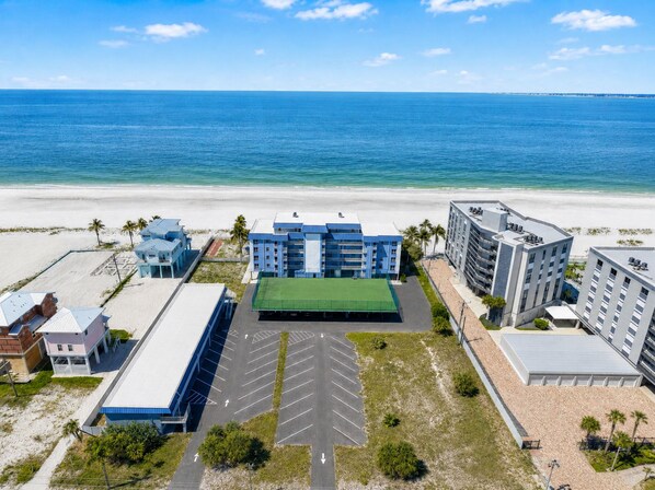 Ein Strandhotel mit mehreren Gebäuden, einem grünen Tennisplatz und einem Parkplatz.