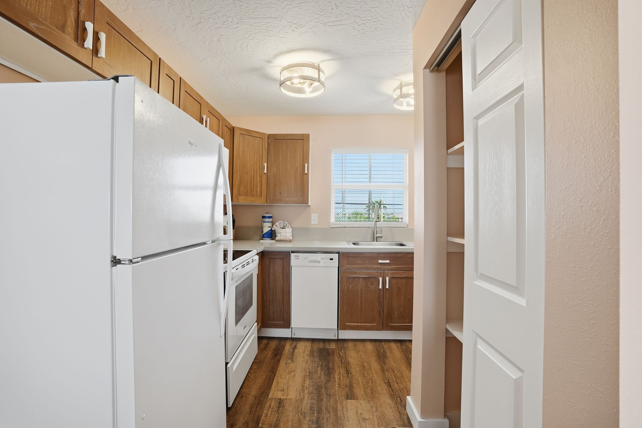 Una cocina con armarios de madera, un refrigerador blanco, un lavavajillas y una ventana con vistas.