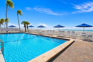 Ein Swimmingpool mit klarem, blauem Wasser, umgeben von Liegestühlen und Sonnenschirmen, mit Blick auf den Ozean.