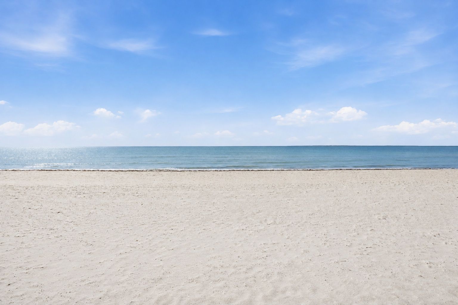 Une vaste plage de sable fin, avec une mer calme et un ciel dégagé.