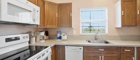 A kitchen with wooden cabinets, a microwave, stove, dishwasher, and a window with blinds.