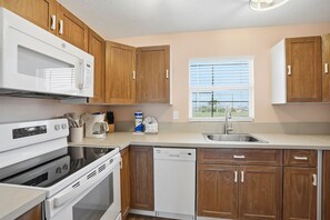 A kitchen with wooden cabinets, a microwave, stove, dishwasher, and a window with blinds.