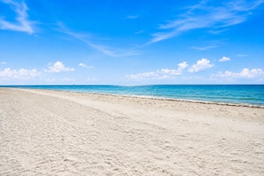 Una playa amplia de arena clara, con cielo azul despejado y mar tranquilo.