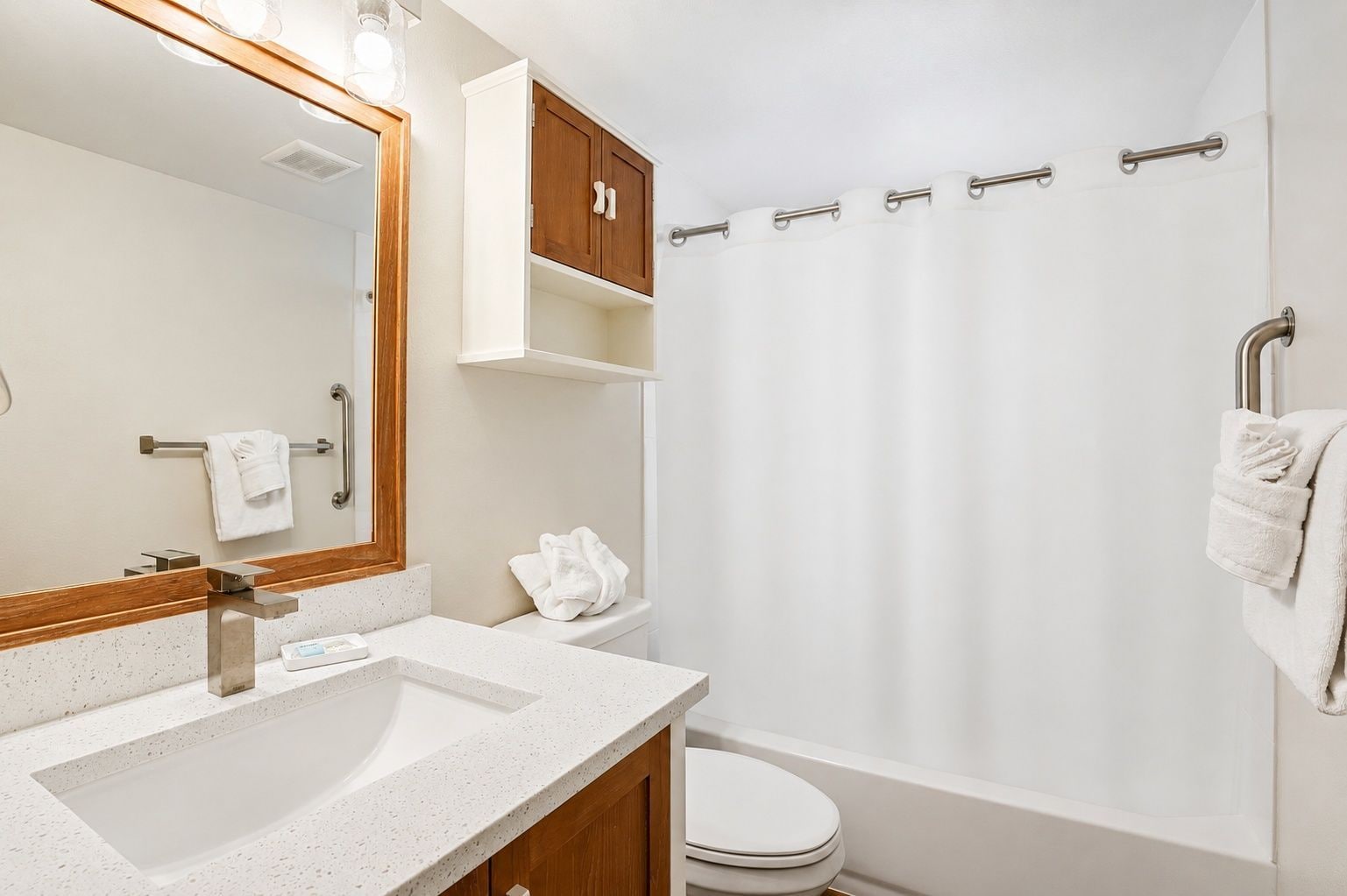 A bathroom with a white sink, a mirror, a wooden cabinet, a toilet, and a shower curtain.