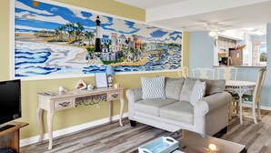 A living room with a large beach-themed painting, a sofa, a coffee table, and a TV.