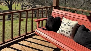 A wooden deck with a red bench, a hanging swing, and a view of trees and grass. - The Redwood Estate - Events on 25 Acres of Serenity (Aubrey)