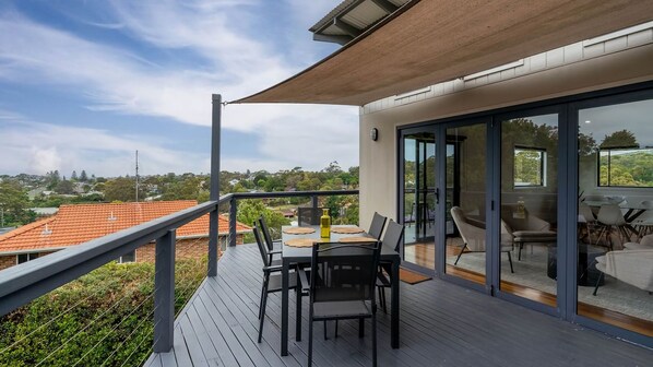 A balcony with a table and chairs, a glass door leading to an indoor area, and a view of the surrounding landscape. - Sea Views set atop a hill in Kiama (Kiama)