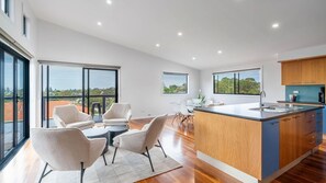 A modern kitchen with a large island, dining area with chairs, and large windows offering views. - Sea Views set atop a hill in Kiama (Kiama)