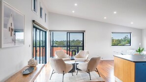 A modern kitchen with a dining area, large windows, and a view of the cityscape. - Sea Views set atop a hill in Kiama (Kiama)