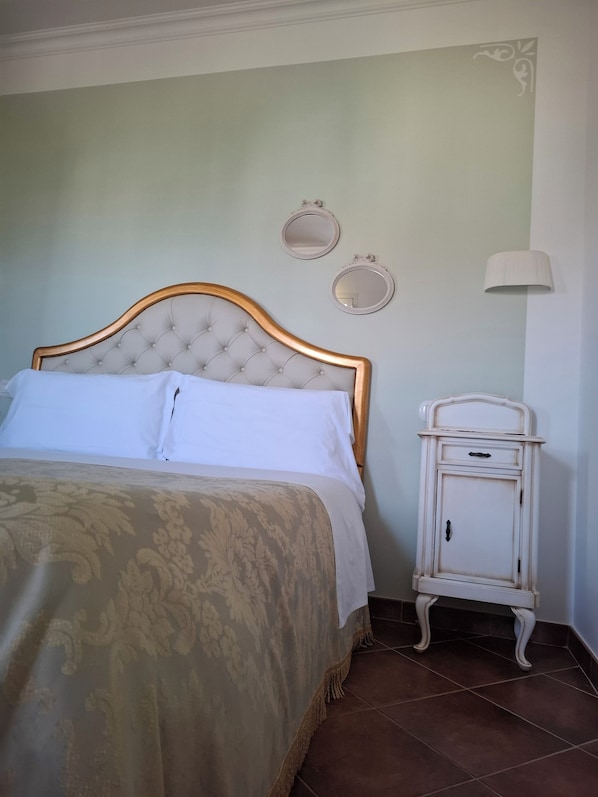A neatly made bed with a tufted headboard, a bedside table with a drawer, and two wall-mounted mirrors.