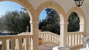 A covered outdoor area with a white sofa, a stone railing, and a view of trees and a body of water. - 4 minutes from the historic center of Ostuni Family apartment with swimming pool (Ostuni)