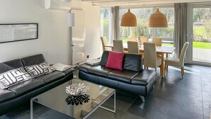 Un salon moderne avec un canapé en cuir noir, une table basse en verre et un coin repas comprenant une table et des chaises.