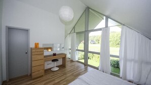 Une chambre à coucher avec une commode en bois, une table de chevet, un grand lit et une fenêtre avec des rideaux.