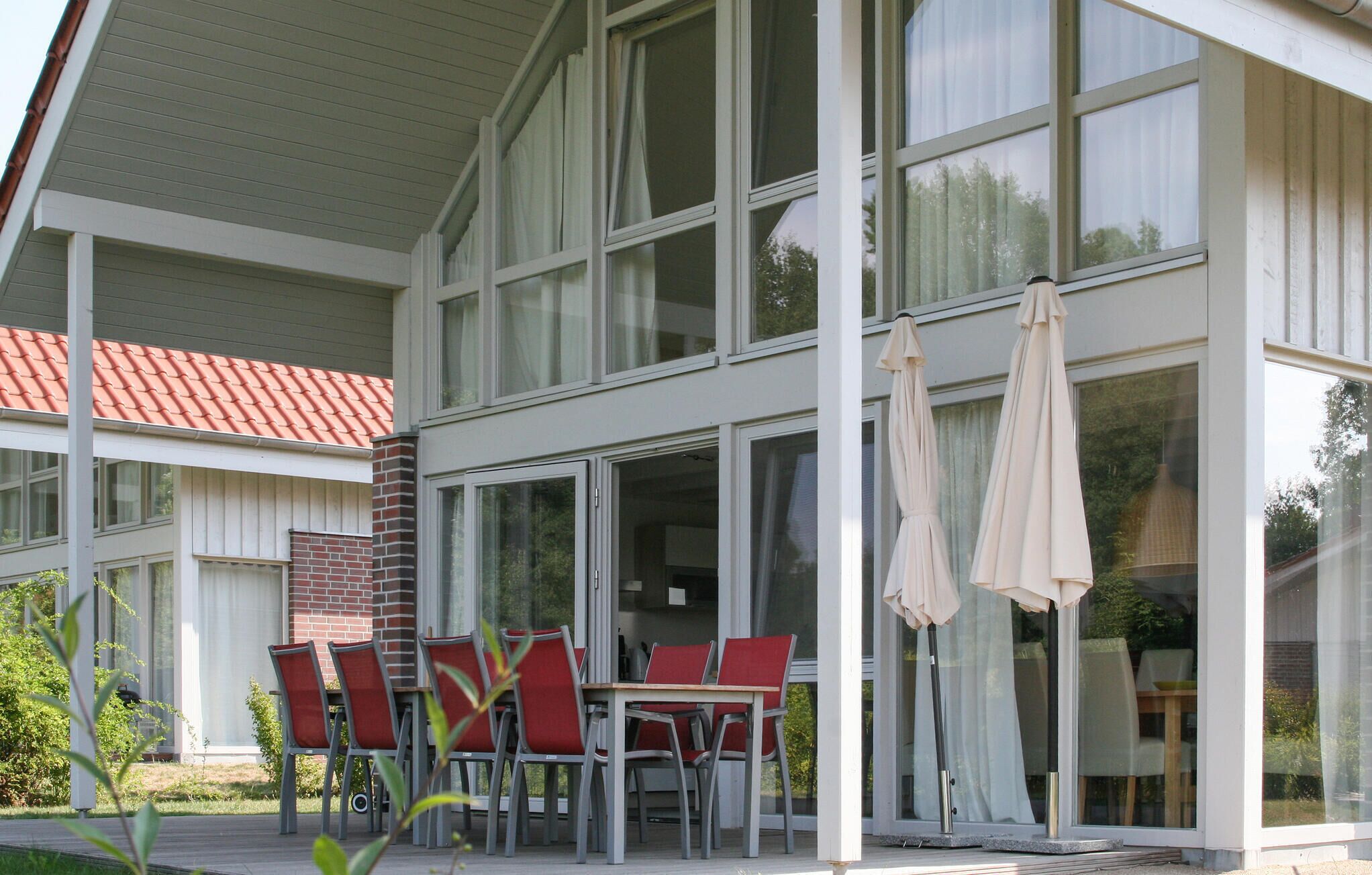 Ein modernes Gebäude mit großen Fenstern und einer überdachten Terrasse mit Sitzgelegenheiten im Freien.