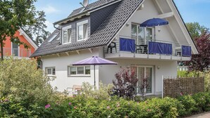 Een huis met twee verdiepingen, een schuin dak, een balkon met blauwe gordijnen en een patio met een paarse parasol.
