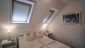 Een slaapkamer met een bed, twee nachtkastjes, een lamp, een lijst met een foto aan de muur en dakramen.