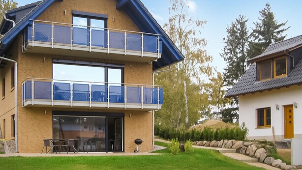 Une maison à deux étages avec un balcon, un barbecue et un petit jardin.