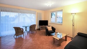 Un salon comprenant un téléviseur, deux fauteuils, un canapé, une table basse et un lampadaire.