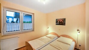 Une chambre avec deux lits, une fenêtre avec des rideaux, un radiateur et un tableau au mur.