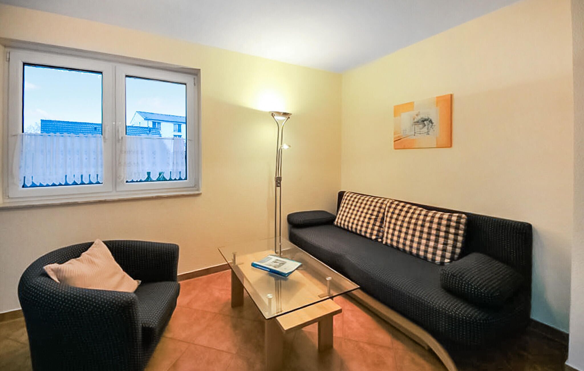 A living room with a sofa, a chair, a glass coffee table, a floor lamp, and a window with a view of buildings.