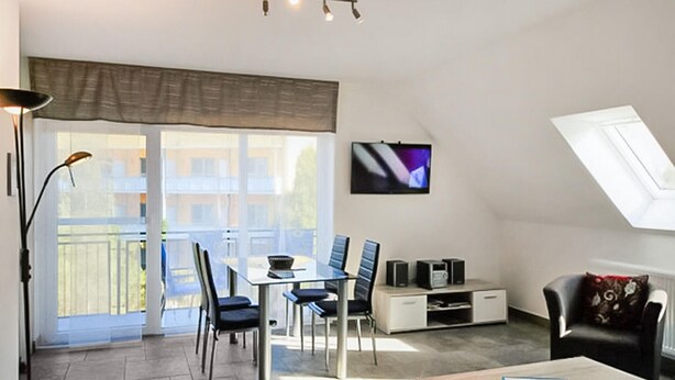 Ein modernes Wohnzimmer mit Essbereich, einer Couch, einem Fernseher und einem Balkon mit Blick auf Gebäude.
