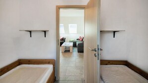 Ein Zimmer mit zwei Einzelbetten, einer Holztür und Blick in einen Wohnbereich mit einer Couch und einem Couchtisch.