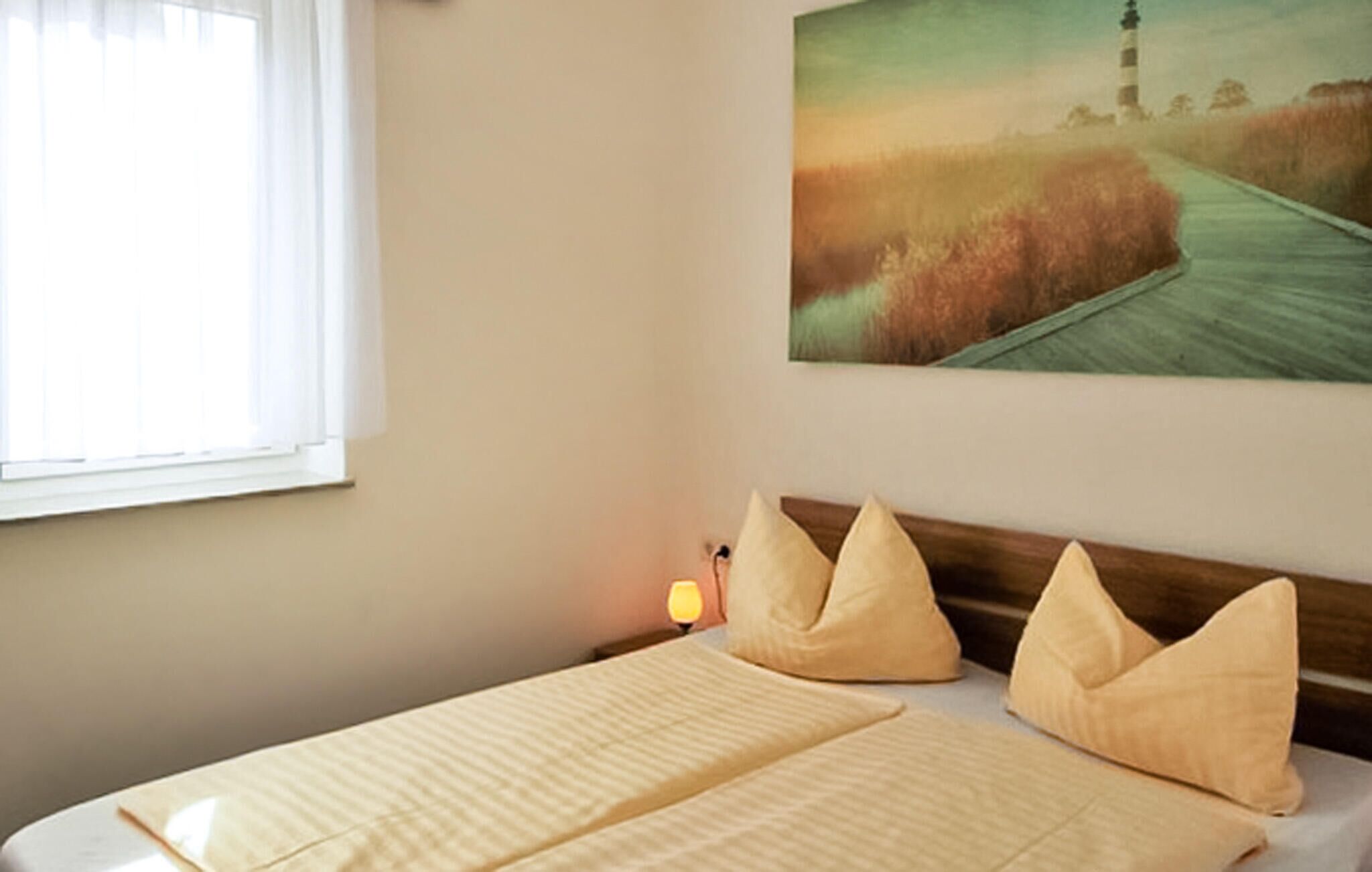A hotel room with a bed, a nightstand, a lamp, and a painting of a lighthouse on the wall.