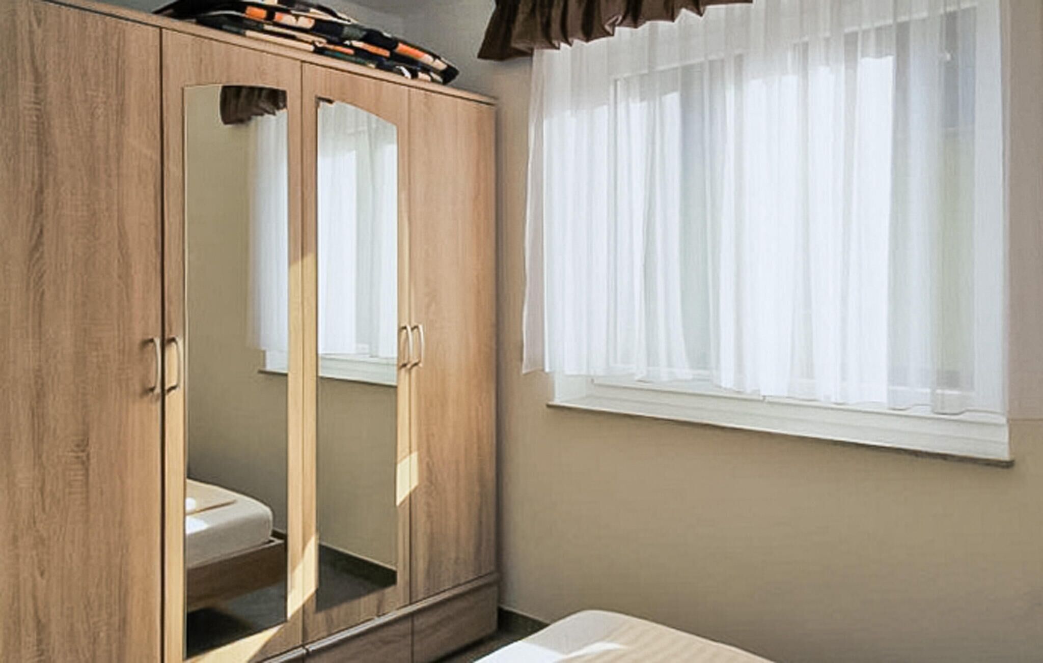 Une chambre avec une armoire en bois, un lit et une fenêtre ornée de rideaux légers.