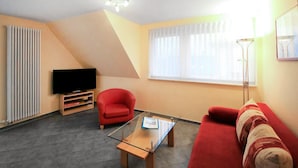 A living room with a red sofa, a glass coffee table, a red armchair, a TV on a stand, and a window with curtains. - 1 bedroom pet friendly apartment in Röbel (Röbel)