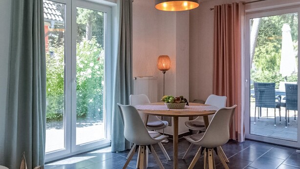 Un coin repas comprenant une table ronde, quatre chaises, un saladier rempli de fruits et un lampadaire.