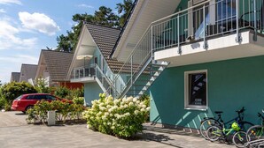 Un immeuble résidentiel à l’extérieur verdoyant, doté d’un toit en tuiles et d’un balcon avec des balustrades en métal.