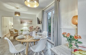 Un espace repas avec une table ronde dressée pour quatre personnes, entourée de chaises blanches.