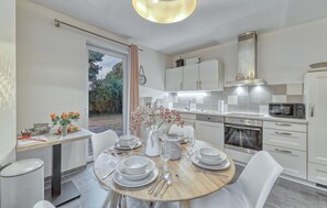 Une cuisine moderne avec des armoires blanches, un four encastré et un coin repas doté d’une table ronde prévue pour quatre personnes.