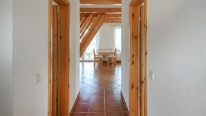 Un pasillo con vigas de madera, suelo de baldosas y un comedor con mesa y sillas al fondo.