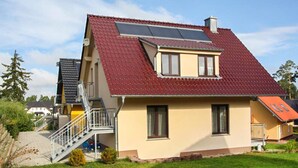 Una casa de dos pisos con techo rojo, un panel solar y una pequeña escalera que lleva a la entrada.
