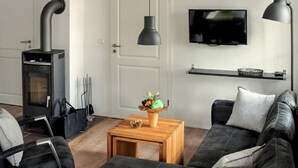 A modern living room with a black leather sofa, a wooden coffee table with a vase of flowers, a TV on the wall, and a fireplace. - Lovely apartment in Röbel with sauna (Röbel)