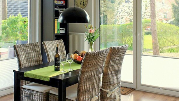 A dining area with wicker chairs, a black table, and a view of the outdoors through large windows. - Lovely apartment in Röbel with sauna (Röbel)