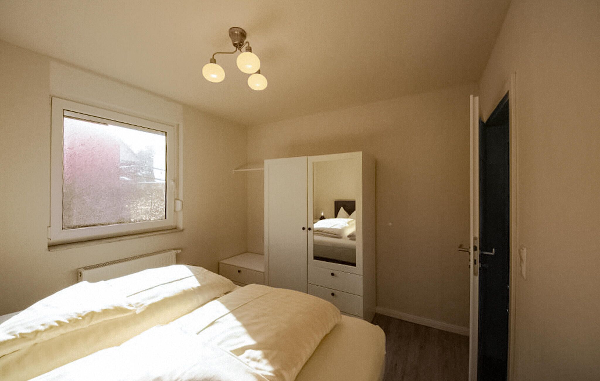 A bedroom with a bed, a wardrobe, a bedside table, and a window.