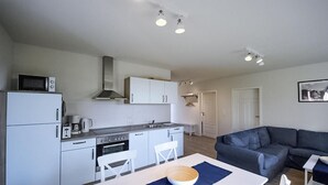 A compact kitchen with white appliances, a dining area with a table and chairs, and a dark-colored sofa in a living area. - Amazing apartment in Röbel with sauna (Röbel)