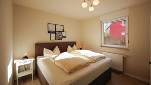 A bedroom with a bed, bedside table, wall art, and a window with a view of a red building. - Amazing apartment in Röbel with sauna (Röbel)