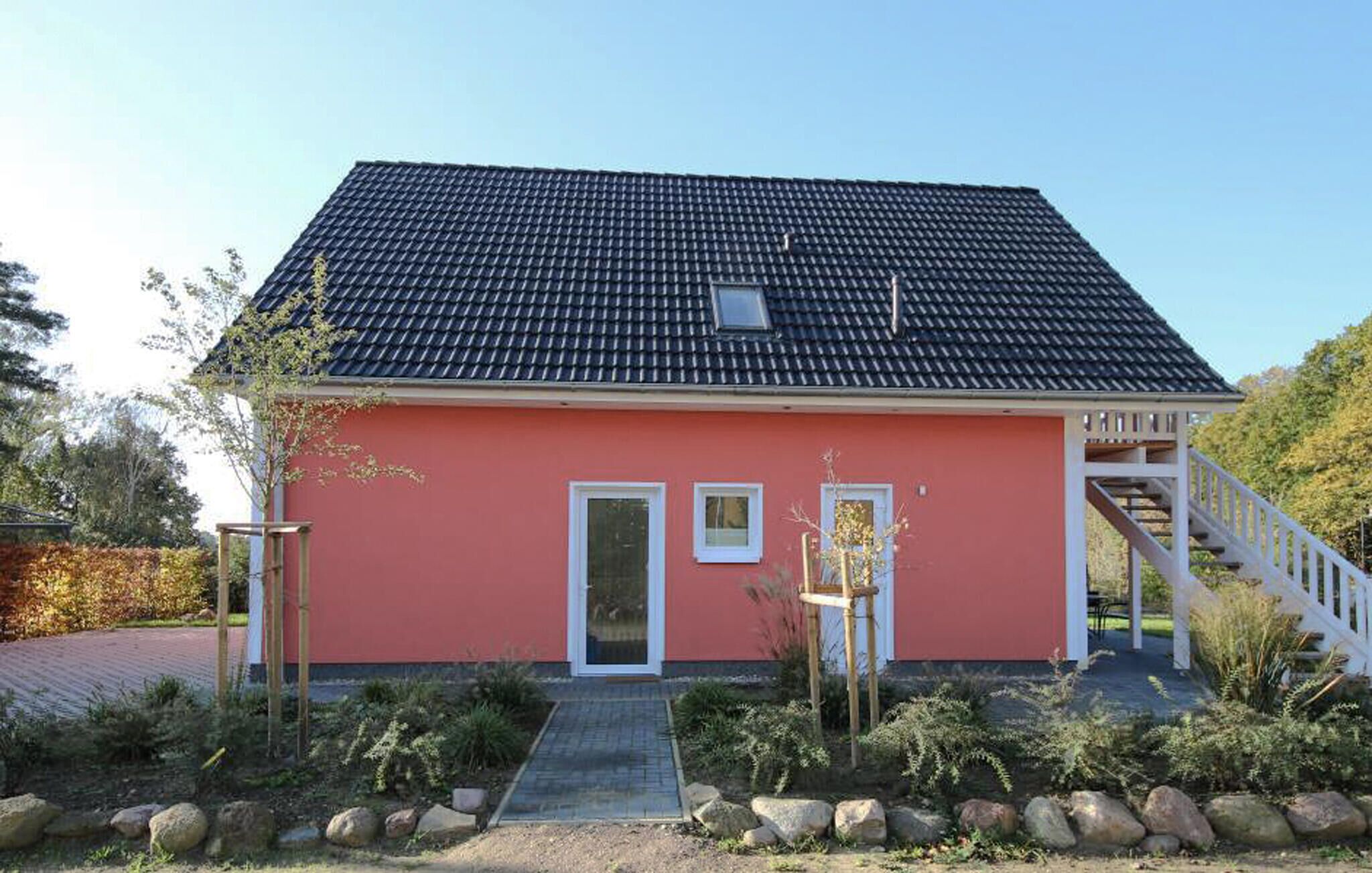 Ein zweistöckiges Haus mit roter Fassade, einem Ziegeldach und einer kleinen Veranda mit Treppe.