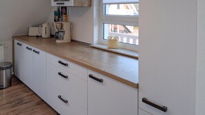 Una cocina con armarios blancos, encimera de madera y ventana con vistas a un edificio.