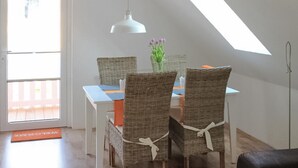 Un comedor con una mesa blanca, sillas de mimbre y una lámpara colgante blanca.