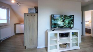 Ein modernes Wohnzimmer mit einem Flachbildfernseher auf einem weißen Schrank, einem Holzschrank und einem Fenster mit Jalousien.