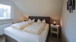 Ein Schlafzimmer mit einem großen Bett, zwei Nachttischen, einem Fenster und einem an der Wand befestigten Bilderrahmen.